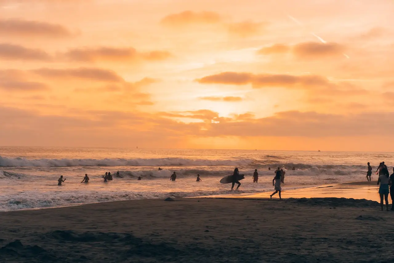Carlsbad State Beach al atardecer con surfistas y suaves olas.